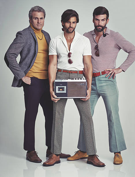 Ready to kick it retro style! A studio shot of three men clad in retro 70s wear holding a cassette player hippie fashion stock pictures, royalty-free photos & images