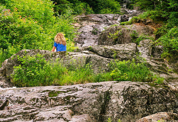 Woman sitting on rocks at waterfall stock photo