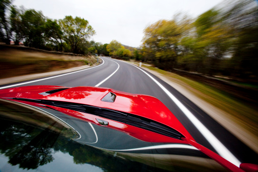 Low angle shot of a red sports car running fast on a tree-lined road creating feelig of speed