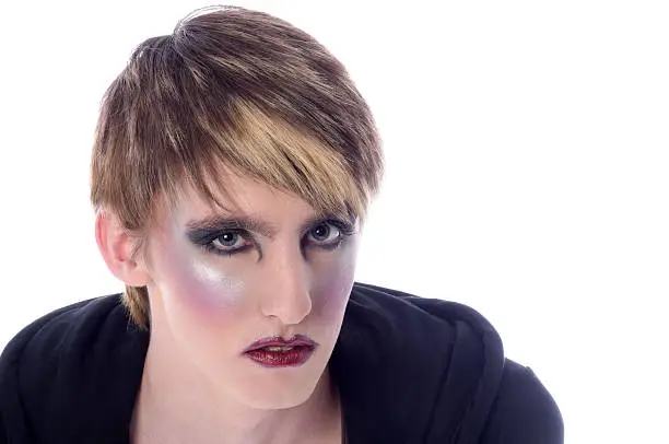 Horizontal studio shot on white of serious young man in glam rock style makeup.