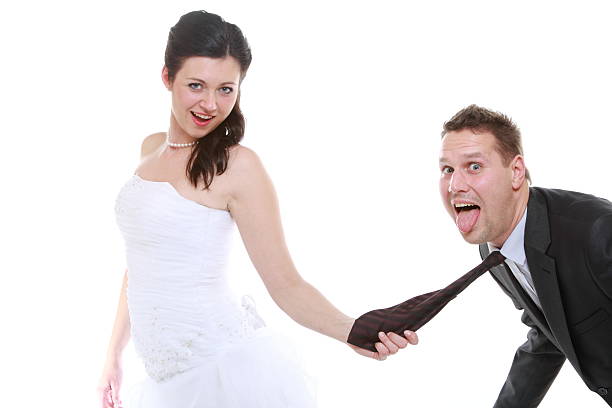 Emancipation idea concept. Humorous funny wedding couple bride and groom - woman pulling the tie of a man, trying to show her domination, isolated