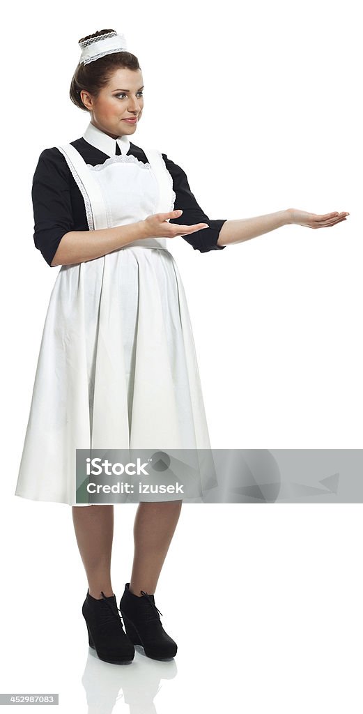 Retro Maid Portrait of smiling vintage maid pointing at copy space. Studio shot, white background. Nanny Stock Photo