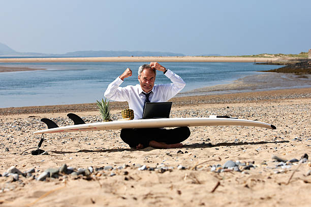 istock Mature businessman laptop on beach and surfboard 452992869