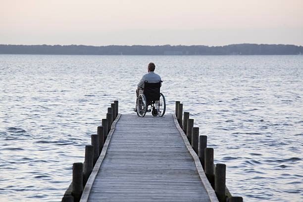 istock Rear view at man in wheelchair on lakeside jetty 453011205