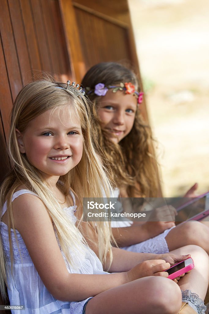 Two girls playing with digital devices. Portrait of two friends sitting outside with smart phone and tablet. Activity Stock Photo