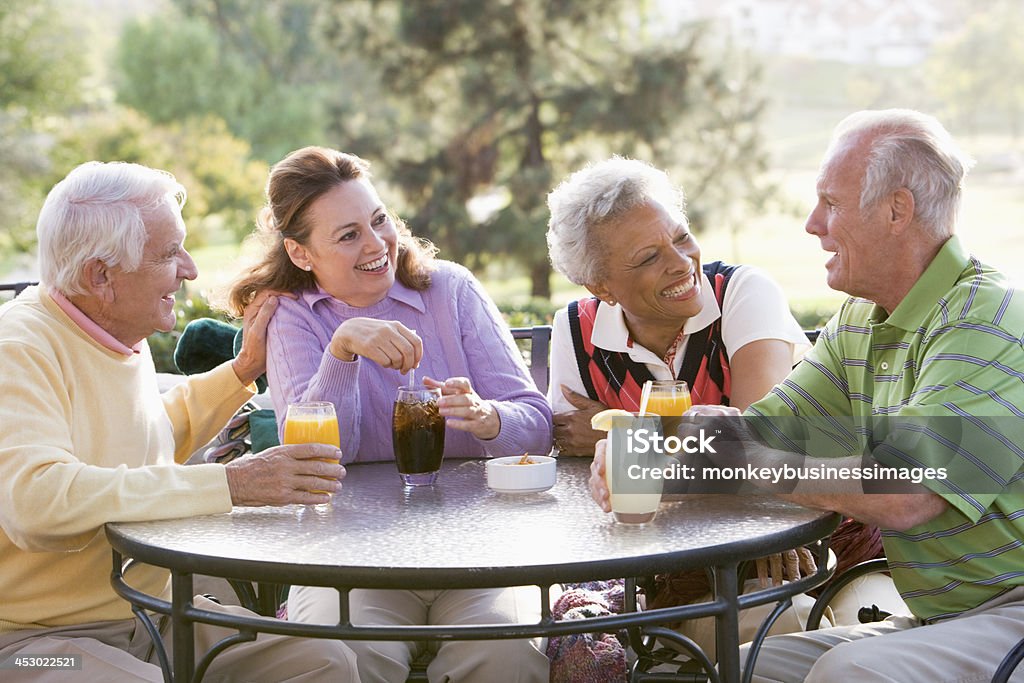 Friends Enjoying  Beverage By A Golf Course Friends Enjoying A Beverage By A Golf Course Sitting Down At Table Chatting Senior Adult Stock Photo