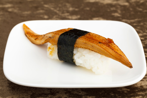 Eel (Unagi) sushi on a white square plate on a brown textured surface.