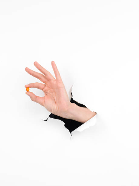 istock hand holding an orange pill through a white paper 453051815