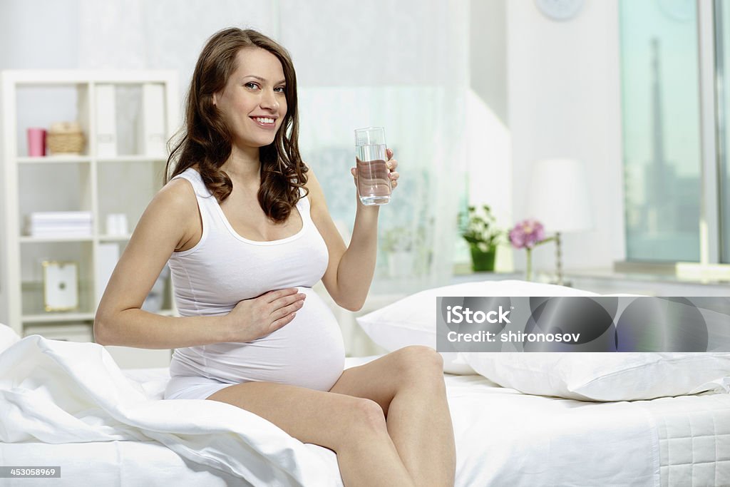 Woman on bed Photo of pretty pregnant woman with glass of water keeping her hands on belly Abdomen Stock Photo