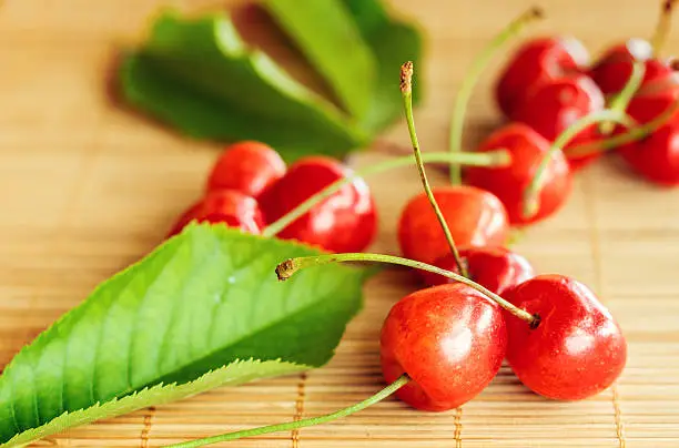 Group of cherries placed near green leaf on bamboo tablecloth.Small depth of field with cross processing.