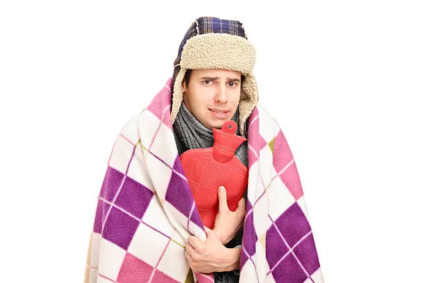 Sick man covered with blanket holding a hot-water bottle isolated against white background