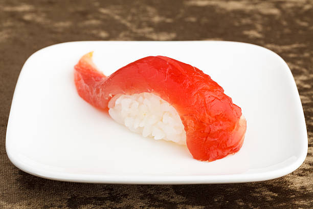 Tuna sushi, Maguro, on a square white plate, on a textured brown background.