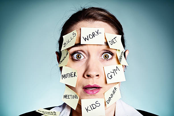 A shocked and overtired woman covered with Post-it reminders for all sorts of tasks looks stunned by how much she has to do. She's seriously over committed.