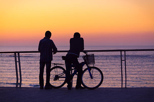 silhouetten von zwei männer und ein fahrrad - siluete stock-fotos und bilder