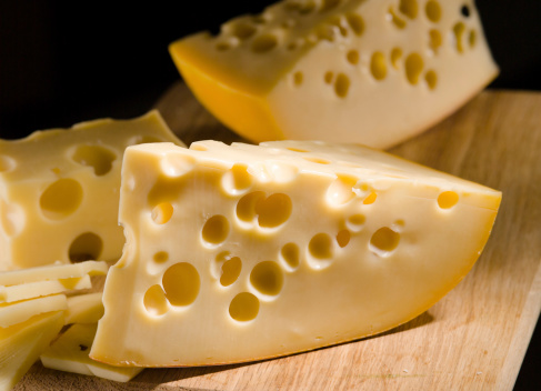 Cheese with big holes on wooden board