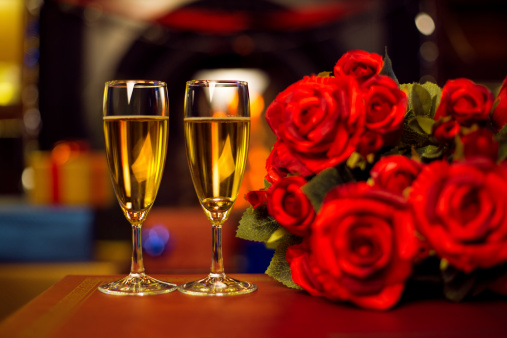 2 glasses in front of a fireplace with a bouquet of roses. There is a wedding ring in the right glass.