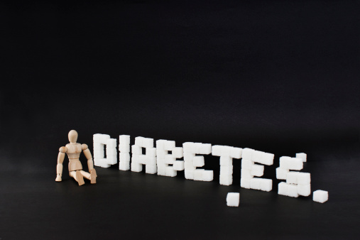 written diabetes with cubic sugar on a black background. Wooden manikin says stop diabetes.