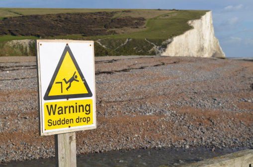 Warning sign showing risk of a sudden drop by a cliffs edge.