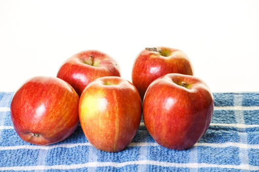 Five red apples on a blue and white towel with a white background