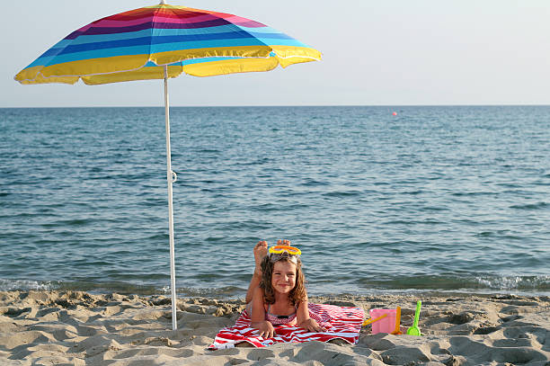 little girl with diving mask lying under sunshade on beach