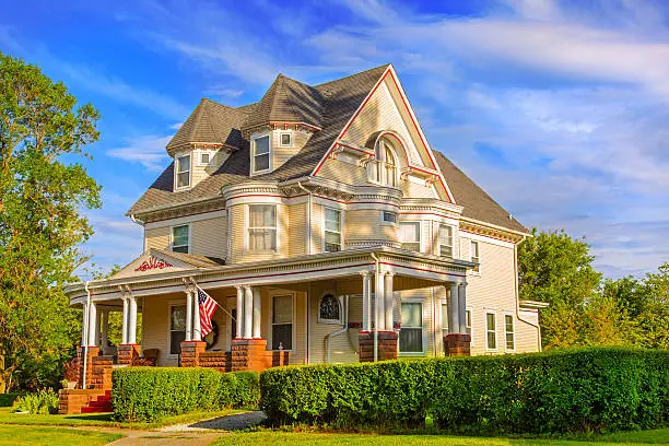 Beautiful Victorian Style home with lush landscaping surrounding the home, blue sky in the background and warm sunset lighting bathing the home in glowing light.