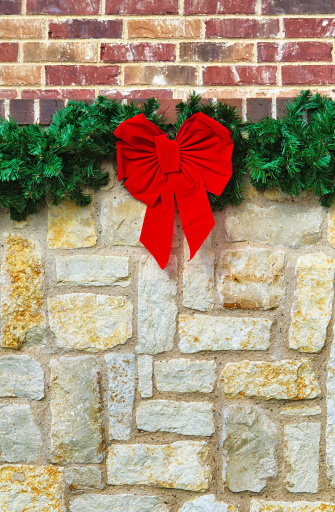 Red Christmas bow and garland hanging on stone fence, brick wall on the background