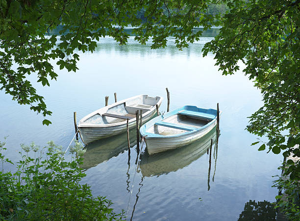 Two rowing boats over water with leaves of trees. Adda, Lombardy Italy..