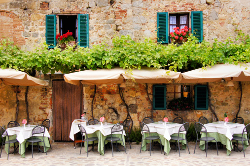 Cafe tables and chairs outside a quaint stone building in Tuscany, Italy