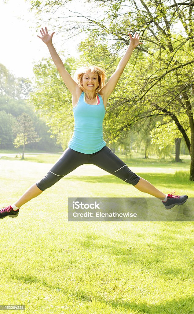 Smiling woman jumping in park Happy female fitness instructor jumping exercising outside at green park Mature Women Stock Photo