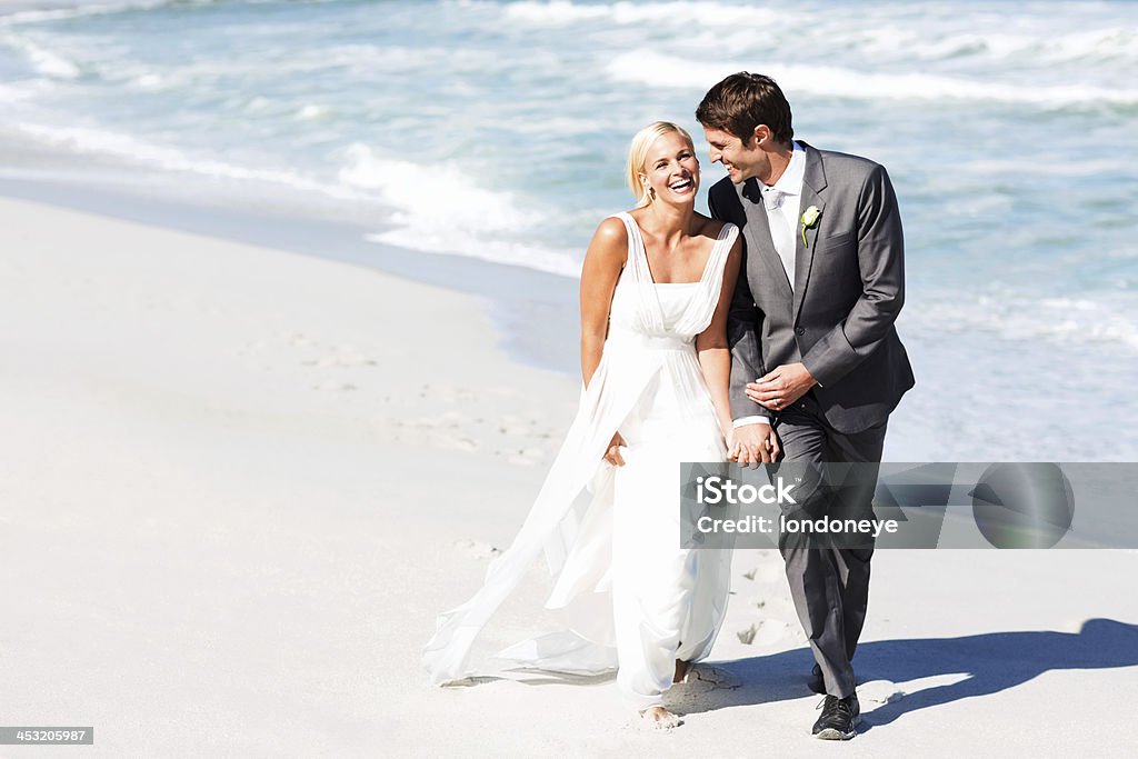 Bride And Groom Walking On Beach Full length of happy bride and groom walking on beach. Horizontal shot. Beach Stock Photo