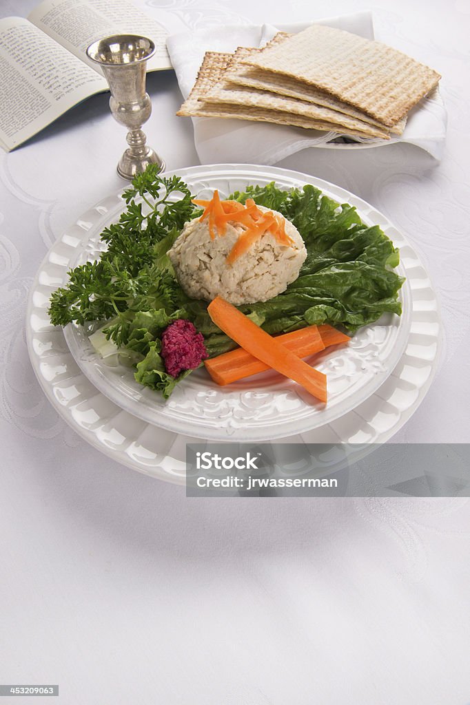 Gefilte Fish with Kidduch Cup, Matzah and Haggadah Traditional Jewish passover food gefilte fish with carrots, parsley, horseradish, and lettuce on white linen table cloth with matzah, Kiddush cup and haggadah in background Beet Stock Photo