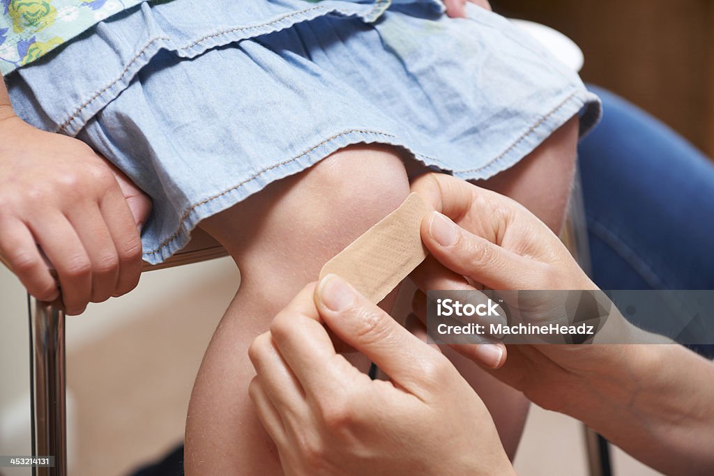 Mother Putting Adhesive Bandage On Daughter's Knee Mum making everything better Adhesive Bandage Stock Photo