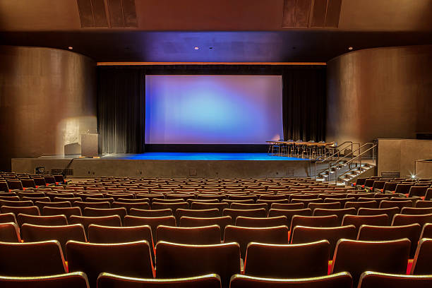 View from the back of an empty auditorium with lights on Empty auditorium with all lights on. Visible scrren in the center of stage. auditorium stock pictures, royalty-free photos & images