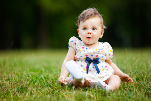 Image of adorable baby girl sitting on grass making funny face, shallow depth of field