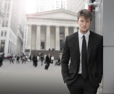 Young attractive businessman outdoors with business district buildings and blurred businesspeople in background