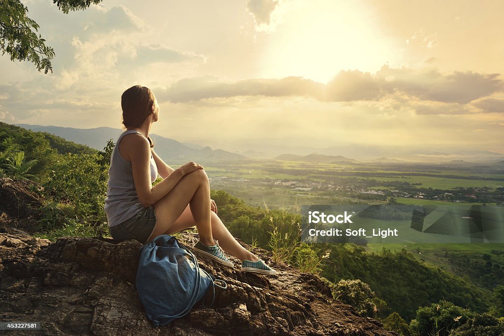 Girl sits on edge cliff and looking at sun valley Girl sits on the edge of cliff and looking at sun valley and mountains Women Stock Photo