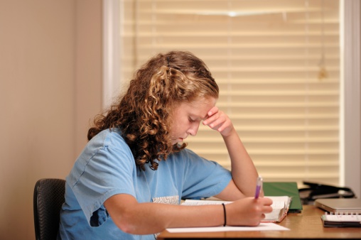 Close up of young teenage girl studying intently at desk with school textbook.