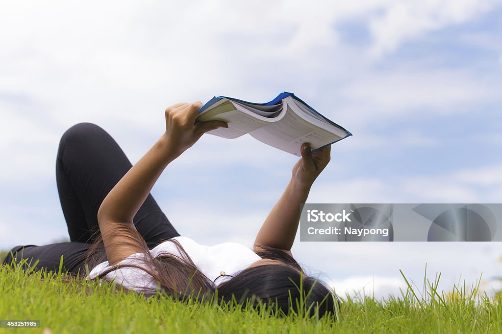 Asian woman using tablet computer Woman reading a book in the park Adult Stock Photo