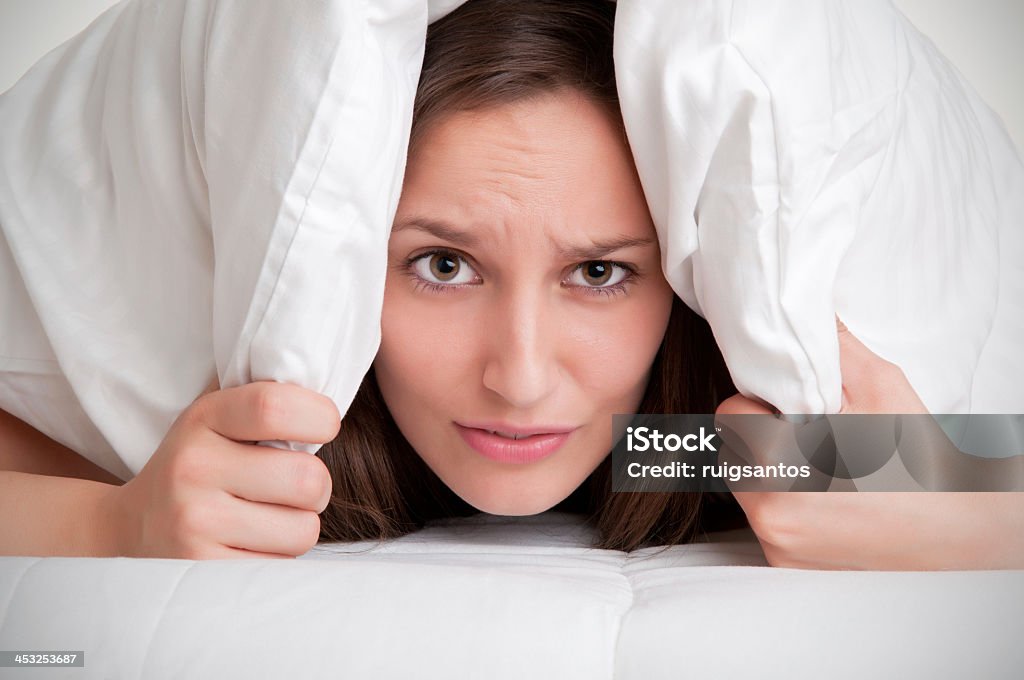 Woman hiding under pillow upon waking up Woman with a pillow over her head, not wanting to get out of the bed, isolated in white Adult Stock Photo