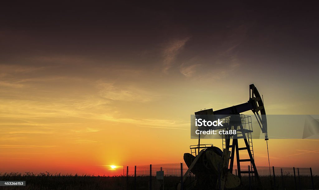 An oil and gas well operating during sunset Operating oil and gas well profiled on sunset sky Fracking Stock Photo