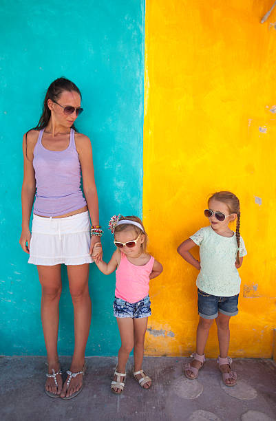 istock Young mother with cute daughters standing near bright colored wall 453274857