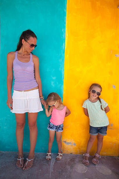 istock Young mother with cute daughters standing near bright colored wall 453274885