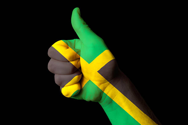 The image shows the national flag of Jamaica, featuring its distinctive gold diagonal cross dividing the green and black fields. The gently waving fabric enhances the bold colors and dynamic geometric design.