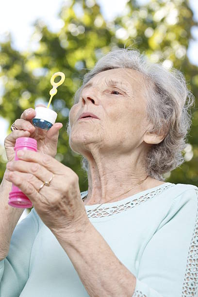 Playful grandmother plays with soap bubbles stock photo