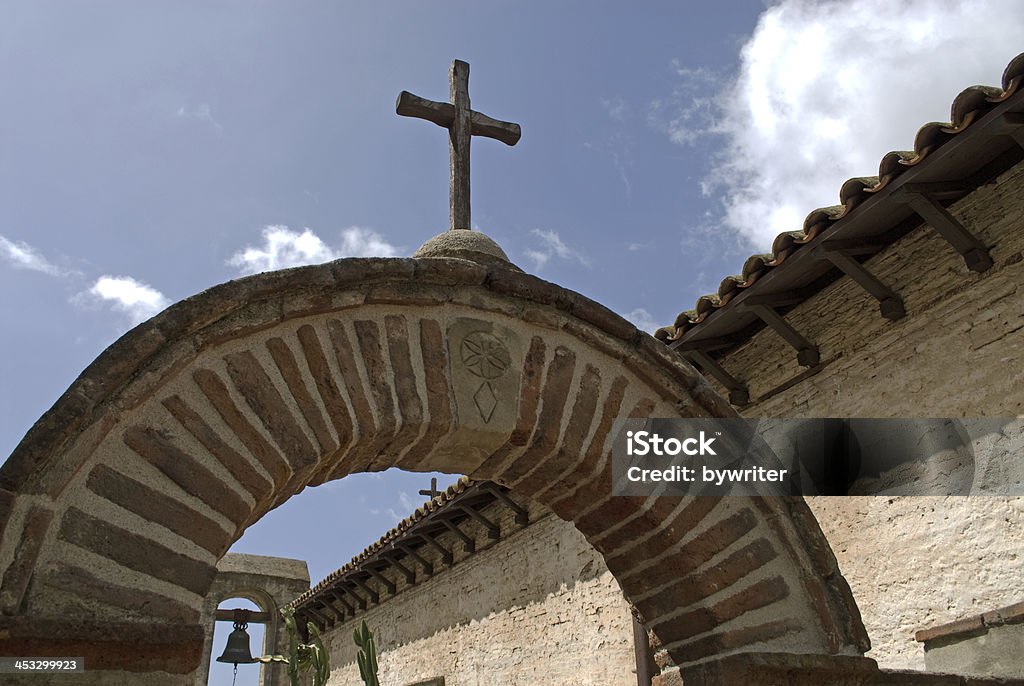 Mission San Juan Capistrano A cross stands on an arched entrance to the Sacred Garden & Bell Wall at Mission San Juan Capistrano. Thousands of people yearly visit the historic mission in San Juan Capistrano, CA. The historic landmark and museum is the seventh of 21 missions founded in Alta California in an effort by the Spanish to extend their territory and convert the natives to Christianity. Arch - Architectural Feature Stock Photo