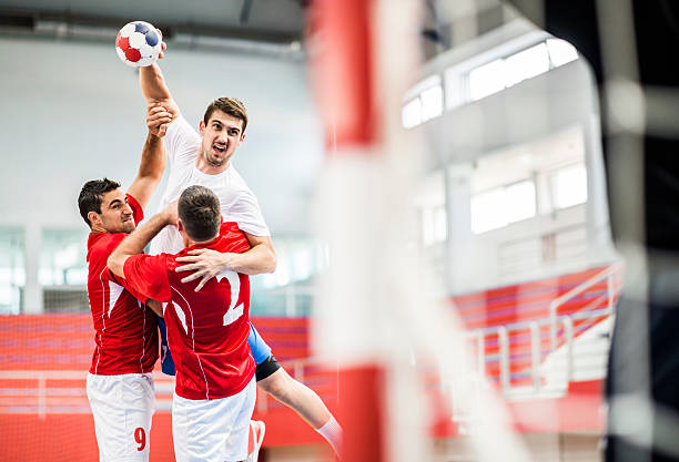 Handball player shooting at goal. Young handball player is shooting at a goal, while his opponents are holding him.    team handball stock pictures, royalty-free photos & images