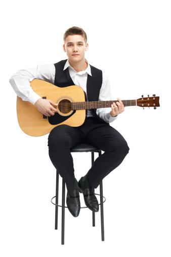 Young man playing on acoustic guitar sitting on a chair isolated on white background