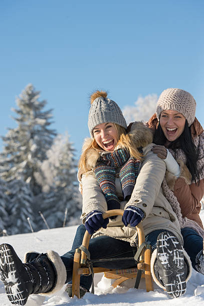 Laughing teenagers sledge downhill in wintertime stock photo