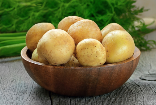 Raw potatoes in bowl on wooden table