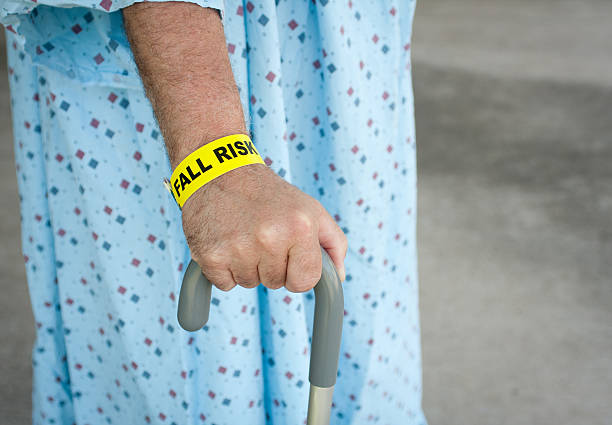 Elderly Man A Fall Risk An elderly man wearing a fall risk bracelet around his wrist at the hospital. Wearing a blue gown and walking with a cane. fall risk stock pictures, royalty-free photos & images